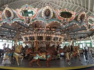 A historic carousel adorned with lights and mirrors containing carousel horse, lion, and rabbit ride figures