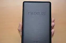 View of the back of a rectangular device held in a hand. The dimpled surface features two prominent words, "Nexus", and "Asus".
