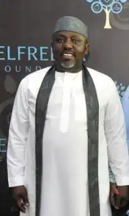Rochas Okorocha in a white dress, wearing a traditional cap