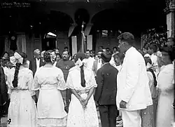 A black and white photograph of Salvador Alvarado addressing a crowd consisting of well-dressed men and women. Alvarado is standing to the left of the photo.