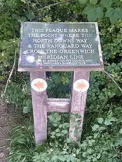 An information board that reads "This plaque marks the point where the North Downs Way & the Vanguard Way cross the Greenwich meridian line"