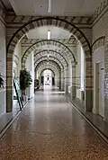 Spine corridor, Liverpool Royal Infirmary (1886–92), strictly utilitarian in style, showing the lack of mouldings and hygienic use of easily cleaned continuous terrazzo floors (normally Waterhouse created borders of mosaic for his terrazzo floors, but the grout would harbour dirt) and white and grey glazed brick walls forming simple patterns, the light colours also shows any dirt
