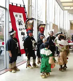 Dark clad people wearing large golden colored hats.