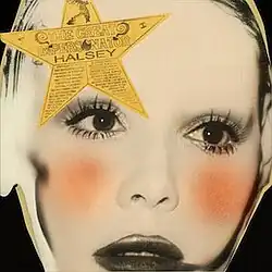 A black-and-white close-up of Halsey's face with orange, doll-like blush. A yellow star has the words "THE GREAT IMPERSONATOR – HALSEY" written on it.
