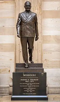 A brown bronze statue of Harry S. Truman. He is walking down steps and wearing a suit with casual shoes. On the pedestal are the words "MISSOURI, HARRY S. TRUMAN" engraved in gold.