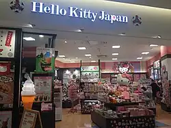 A store with a sign labeling it as a "Hello Kitty Store". Inside the store are many pieces of Hello Kitty merchandise, including toys, fashion, and food.