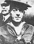 Head and shoulders of a white man wearing a flat sailor's cap, a sailor suit with scarf tied around the neck under the collar, and a star-shaped medal hanging from a ribbon around his neck.