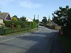 Semi-suburban village road, with the copper-clad church spire in the distance.