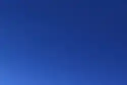 A section of blue sky, featureless other than some light in the lower left corner