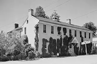 A long two-story building with many windows and ivy creeping up its walls, in black-and-white.