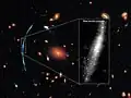 Background galaxy has been gravitationally lensed by the intervening galaxy cluster.[29]