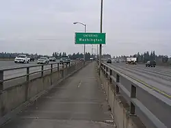 View of a narrow concrete pathway between freeway lanes, separated by a concrete barrier topped with metal railings.