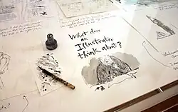 Photograph of a display case containing an ink pot and pen with an illustration of Quentin Blake and the words "What does an illustrator think about?"