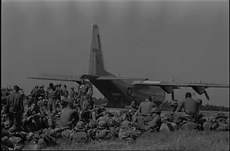 Troops from the 101st Airborne Division are pictured sitting in the grass at the Oxford airfield as a large military cargo aircraft unloads a Jeep