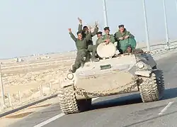 Six uniformed soldiers waving from an armoured vehicle on a highway