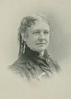 B&W portrait photo of a woman with her hair pulled back into ringlets, wearing a dark jacket.