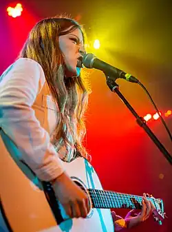 Woman performing onstage against a purple background