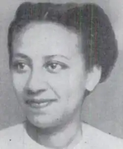 A smiling young Black woman, hair parted center and braided back, wearing a white top with a crew-style neckline