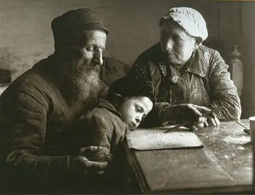 Wolf Nachowicz, the gravedigger, teaches his grandson to read, while the boy's grandmother looks on with pleasure. (Biala Podlaska, Lublin province).