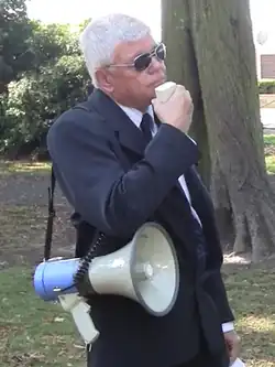 Saleam standing at a nationalist rally outside, holding a megaphone, and wearing sunglasses
