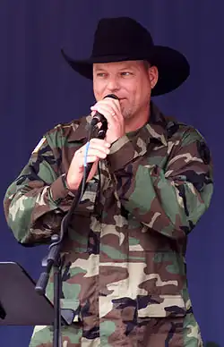 John Michael Montgomery, dressed in camouflage and a black cowboy hat, and singing into a microphone