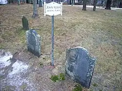 Two gravestones partly covered with moss and a small sign which reads "John Alden Burial Place"