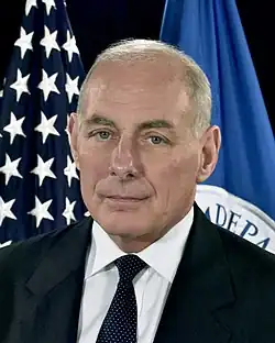 A portrait photograph of John Kelly, an old man in a black suit.
