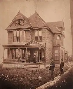 Victorian home with family posed outside, on porch and in windows.