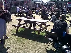 TT rider John McGuinness awaiting a press interview at a picnic bench in the public catering area at the rear of the TT Grandstand during 2013 TT races, with Mrs McGuinness standing to left