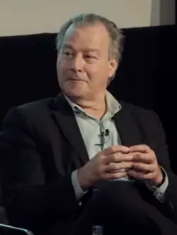 Half-length photo of Jonathon Green sitting on a chair while holding his fingers together