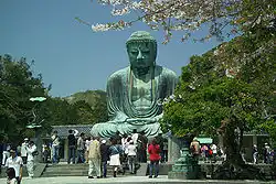 A large Buddha statue in bronze with visitors in front