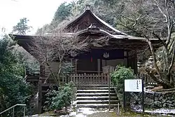 Frontal view of a wooden building with white walls and undulating gable in line with the eaves and below a normal gable.