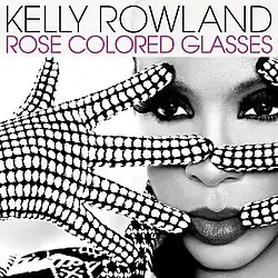 A woman stands with only her face visible. She is wearing polka-dot gloves on her hands which she is holding in front of her face in a spread fashion. The image is black and white. In the foreground at the top, in black text, it reads the artist's name (Kelly Rowland). Directly beneath this it reads the name of the song, in pink text, "Rose Colored Glasses".