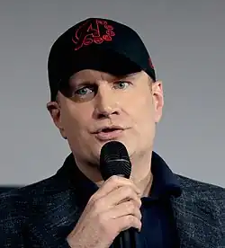 Kevin Feige speaking at Marvel Studios' panel at the 2019 San Diego Comic-Con wearing a black hat with a red Avengers insignia.