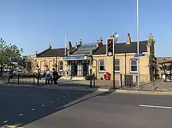 A cream-brick large single-storey building as viewed from across the street, with the view partially blocked by a lamppost and traffic light. In the centre of the building's slanted roof is a decorated glass section with a canopy extending over the door way. A sign on this canopy reads "King's Lynn".