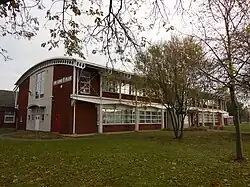 A two-story modern building of red brick and white-painted metal with glass windows and a curved white roof, with "King George V College" visible on one side.