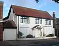A converted house whose downstairs windows and entrance door are covered with white-painted panels. The three upper-storey windows are glazed and have brown frames. An entrance porch is carried on spindly columns.