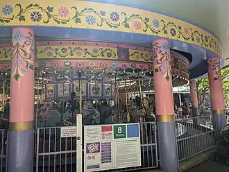 A historic carousel inside a shelter building both painted in yellow, pink, and purple pastel colors