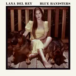 A picture of Del Rey in a yellow dress sitting with two dogs by her sides on a wooden porch in front of the banisters. The picture is surrounded by a white outline with the text "Lana Del Rey" and "Blue Banisters" written in black.