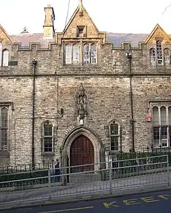 Part of a building with an arched entrance over which is a statue in a niche