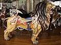 A stationary lion carousel figure with carvings of cherubs on either side of its saddle on a historic carousel