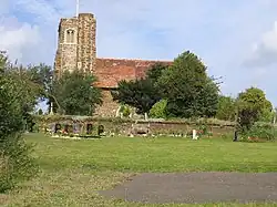 A stone church seen from the south, with a tower and stair turret to the left, and the red tiled body of the church to the right
