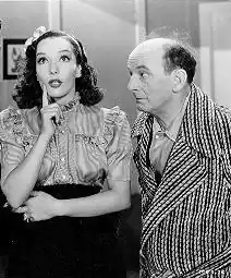 Black and white film still showing Lupe Vélez looking thoughtful while talking and Leon Errol in a dressing robe looking at her incredulously in a scene from Mexican Spitfire (1940)