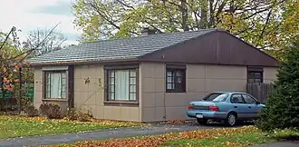 A brown house with the same grid-pattern siding and a blue car parked in a driveway on the left.