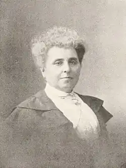 B&W portrait photo of a woman with her white hair in an up-do, wearing a white blouse and dark jacket.
