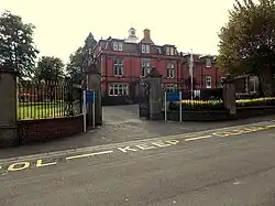 some large gates, with a red brick building with cupola beyond