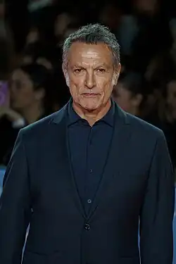 Cosimo Fusco wearing a dark blue shirt and dark blue blazer, looking directly at camera with a slight scowl