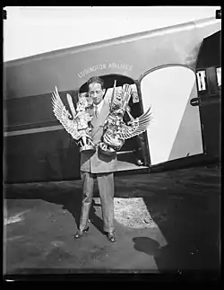Film director Charles Tillyer Trego standing in front of a Ludington Aielomes airplane holding two trophies