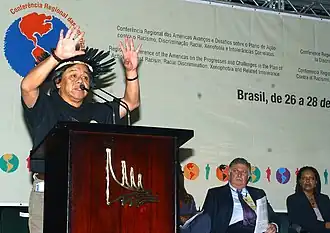 Indigenous leader speaking at a conference with his hands up