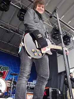 Martin Johnson wearing a black outfit with an electric guitar smiling